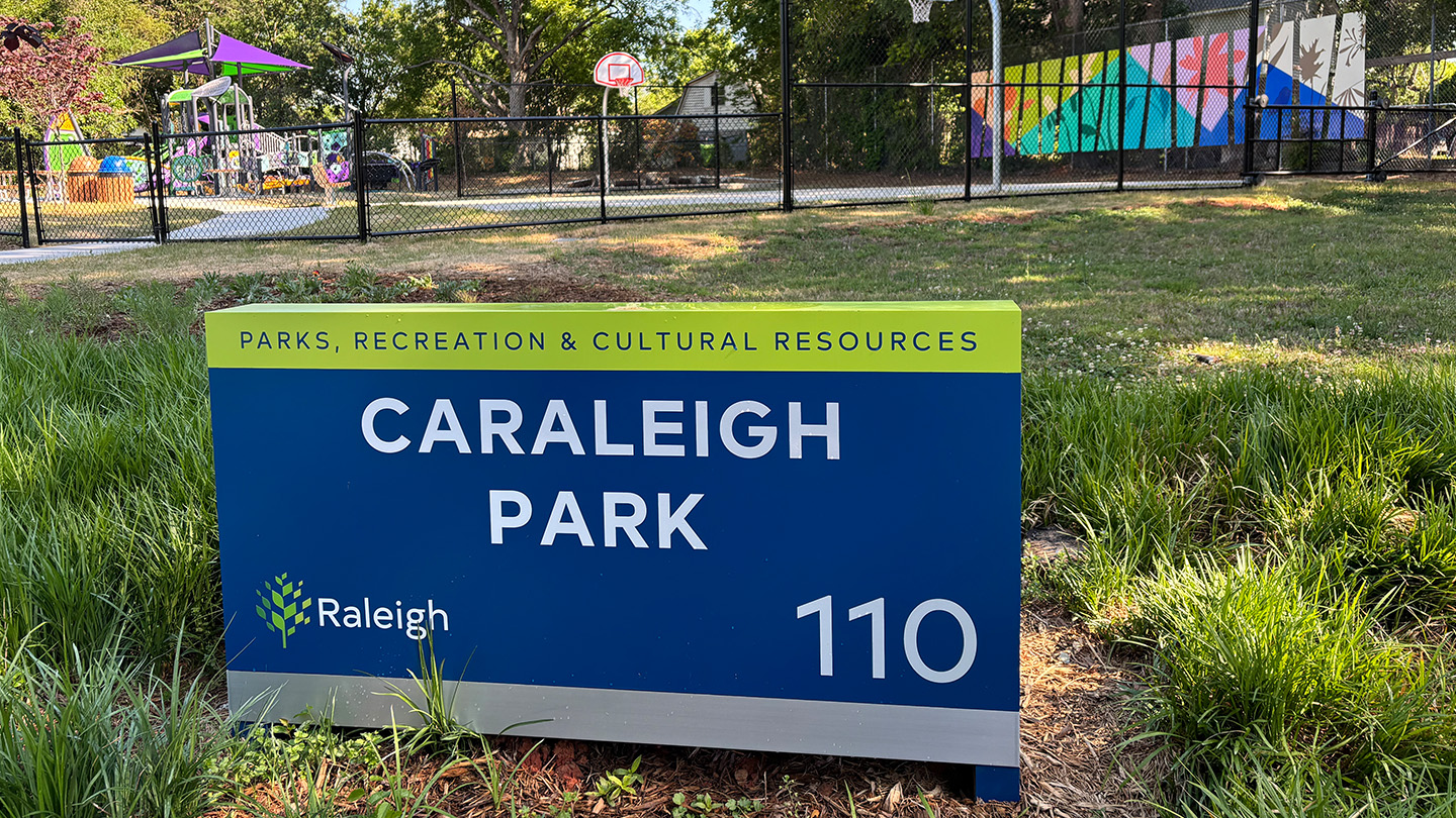Closeup of a sign saying Caraleigh Park. Artwork can be seen in the background.