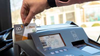 A hand holding a GoPass swiping it through the fare machine on a bus