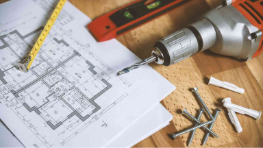 Image of plans, pencil, level, drill, and screws laying on a table