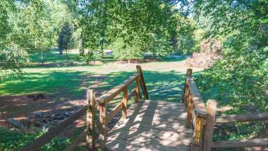 Wooden steps leading to large grassy area surrounded by trees.