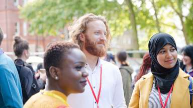 Three people of different ethnic backgrounds standing around with lanyards on