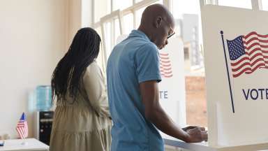 Two people stand at voting booths filling out ballots