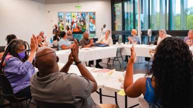 A group of people clap while sitting at tables during a public meeting