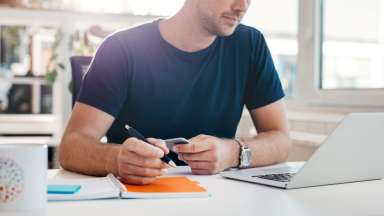 man-at-desk-holding-pen-and-looking-at-laptop