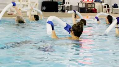 people in a pool with gloves and pool noodles