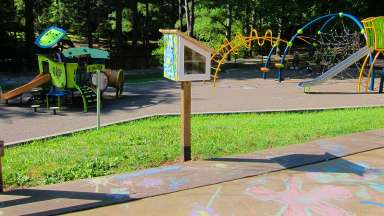 a box on a post filled with chalk sits next to pavement covered in mural and chalk art
