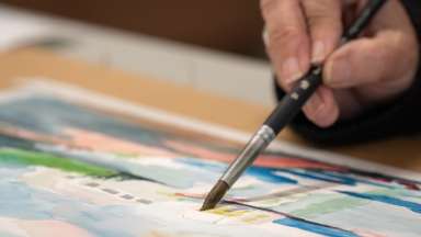 Paint brush applying watercolor paint to paper.
