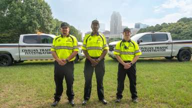Three members of the Civilian Traffic Investigation team and their pickup trucks with skyline behind