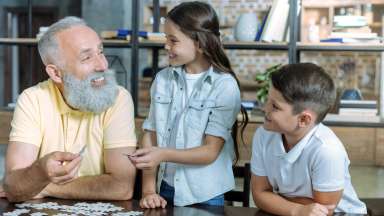 a grandparent smiling while doing a puzzle with their grandchildren