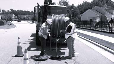 workers standing over open manhole in front of a work truck