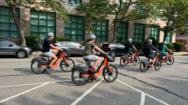 five people ride on orange electric bikes on a Downtown Raleigh street