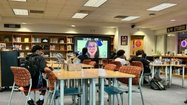 students sitting at open tables in front of meeting projector