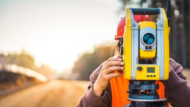Site Survey - Surveyor standing behind and looking through survey equipment