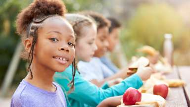 4 children sitting at a table outdoors enjoying food