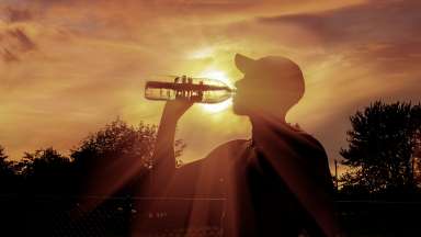 Person drinking water bottle with sun in background