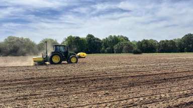 a tractor plowing a field with dust coming up behind it