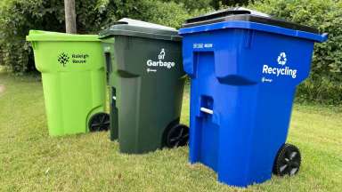 Solid Waste Services yard waste bin (lime green), trash bin (dark green), and recycling bin (blue)