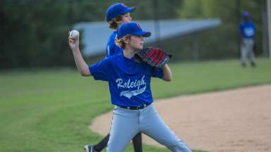 a baseball player throwing a ball while wearing a blue Raleigh Parks jersey