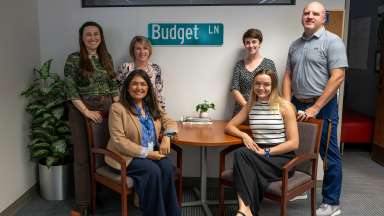 Five members of the Raleigh budget team with "Budget LN" street sign on the wall behind them