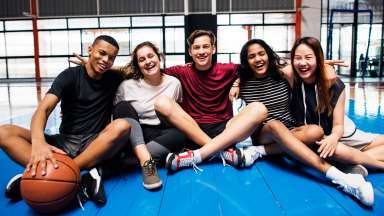 a group of teens, one with a basketball, smiling while sitting