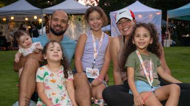 a family of 6 sitting on the grass at an outdoor event smiling