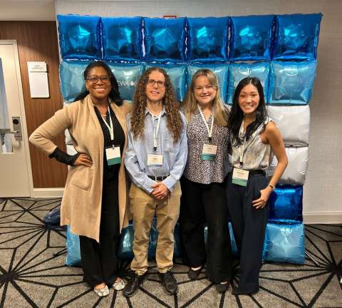 Group picture of four team members standing in front of balloon sign