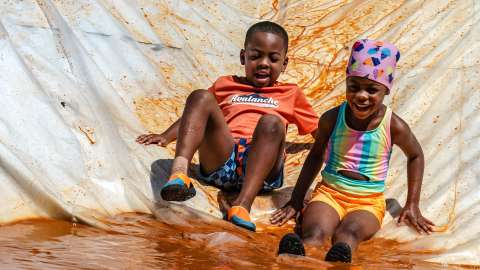 two smiling children sliding down the mud slide