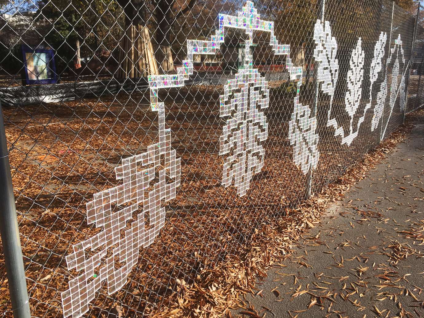 iridescent tiles placed into the holes of chain linked fence create the shape of oak leaves