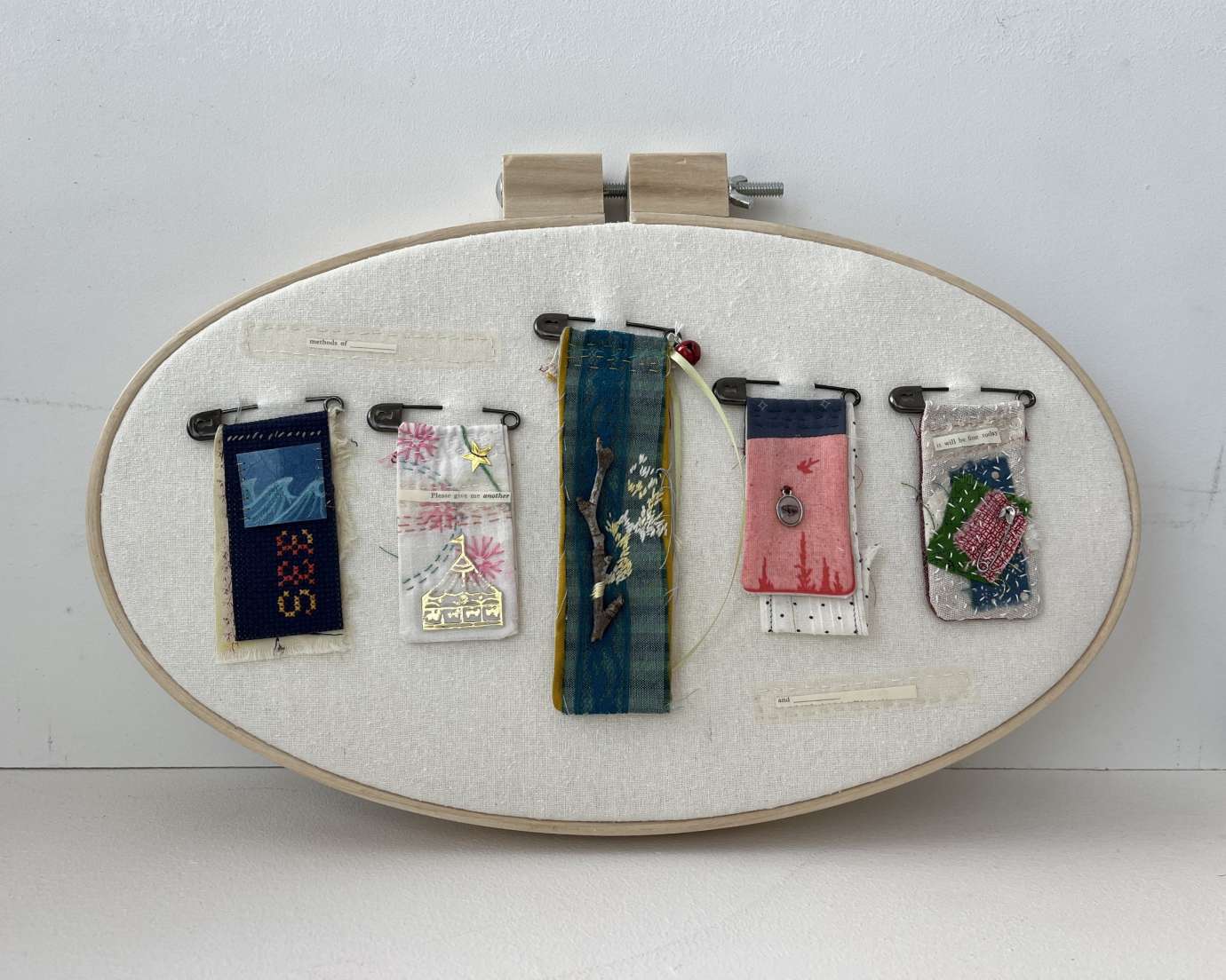 Oval embroidery hoop with cream fabric and small embroidered images pinned at the top. 