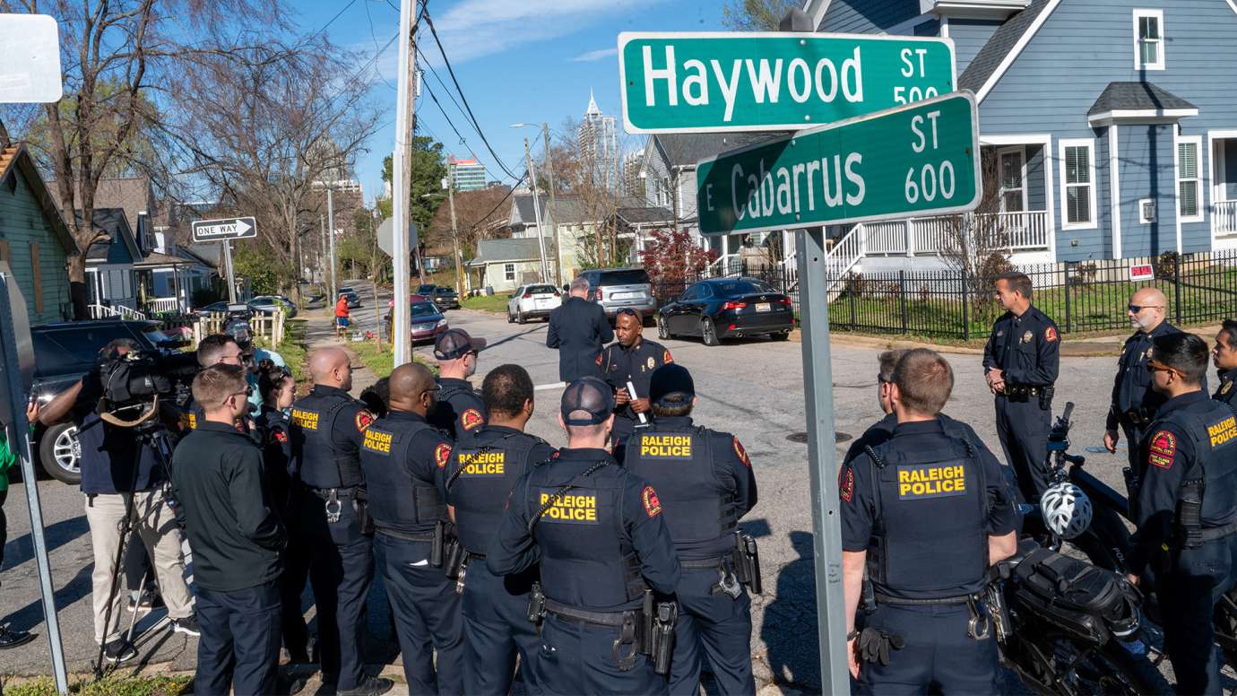 Raleigh officers gather at the corner of Haywood and Carbarrus Streets before speaking to residents. A video camera is recording the discussion.