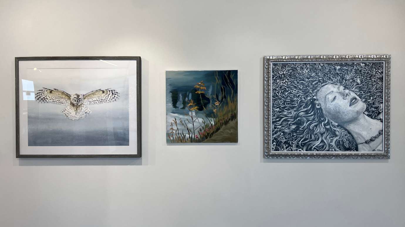 Three paintings installed in the gallery, from left to right: an owl in flight, an abstracted landscape with orange flowers, and a portrait of a girl lying down with her hair spread out around her