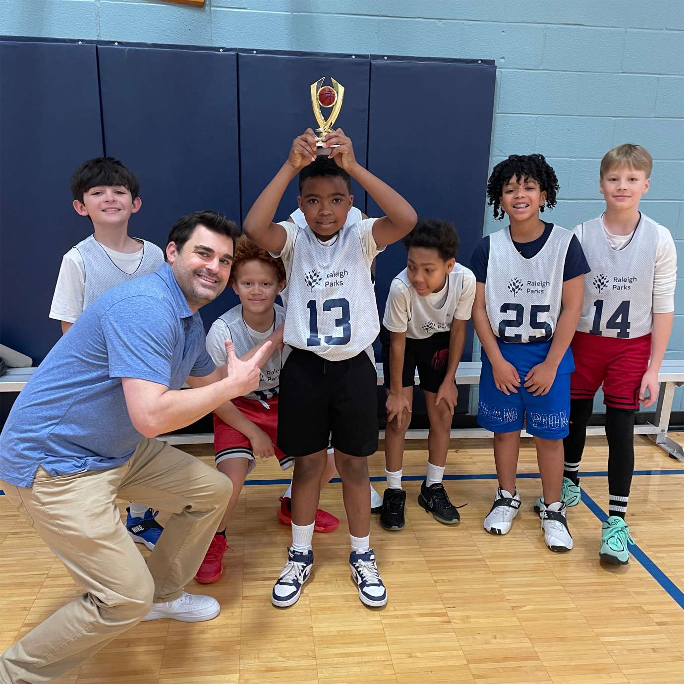 a child smiling with their teammates and a trophy for winning the sportsmanship award