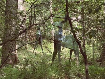 Silouette of folded metal deer in a shaded wooded area. 
