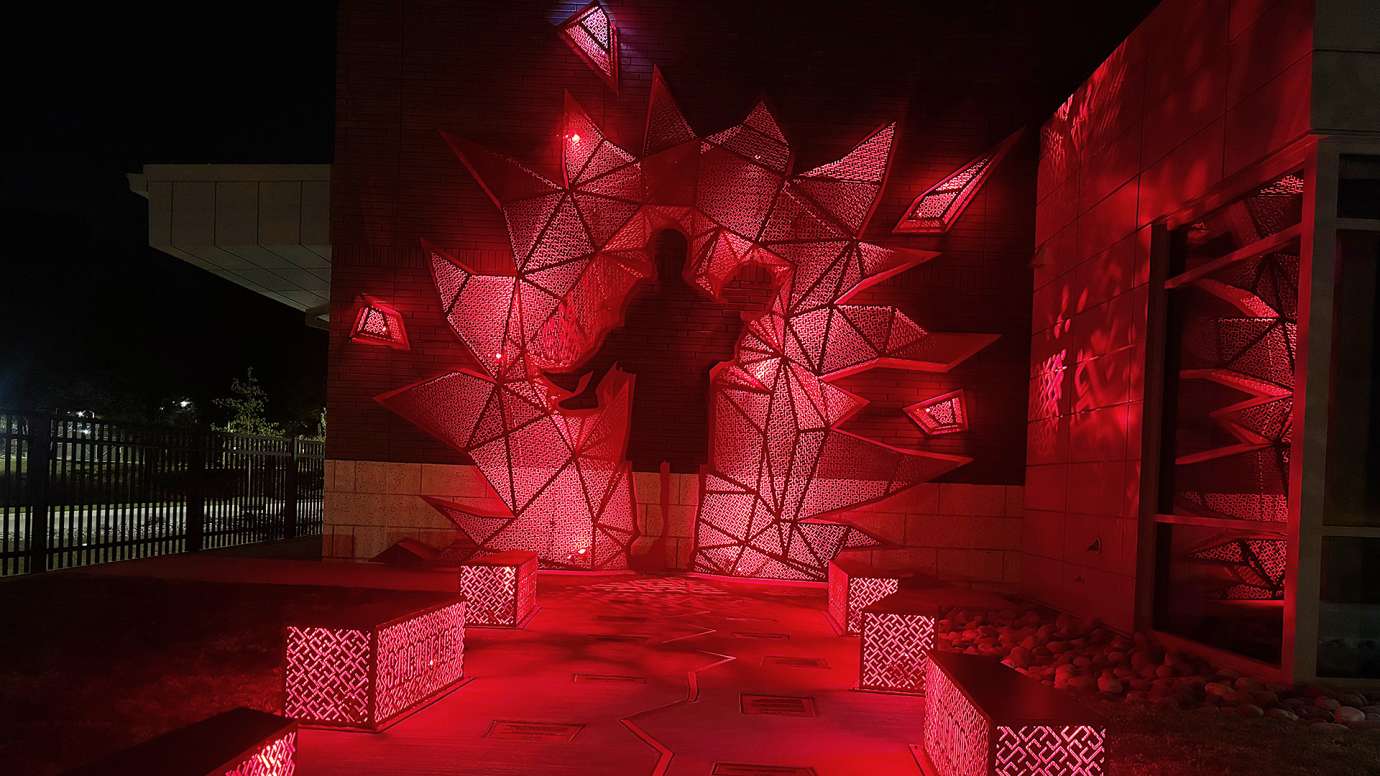 The sculptures and benches of the artwork glow red in a night time shot.
