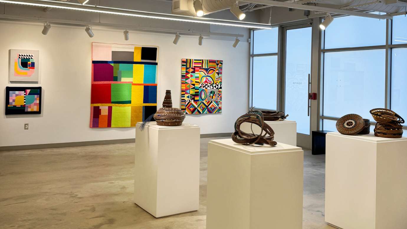 Fiber works by Michelle Wilkie displayed on the wall, with basketry and sculpture by Shakeeka Brooks on pedestals in the gallery