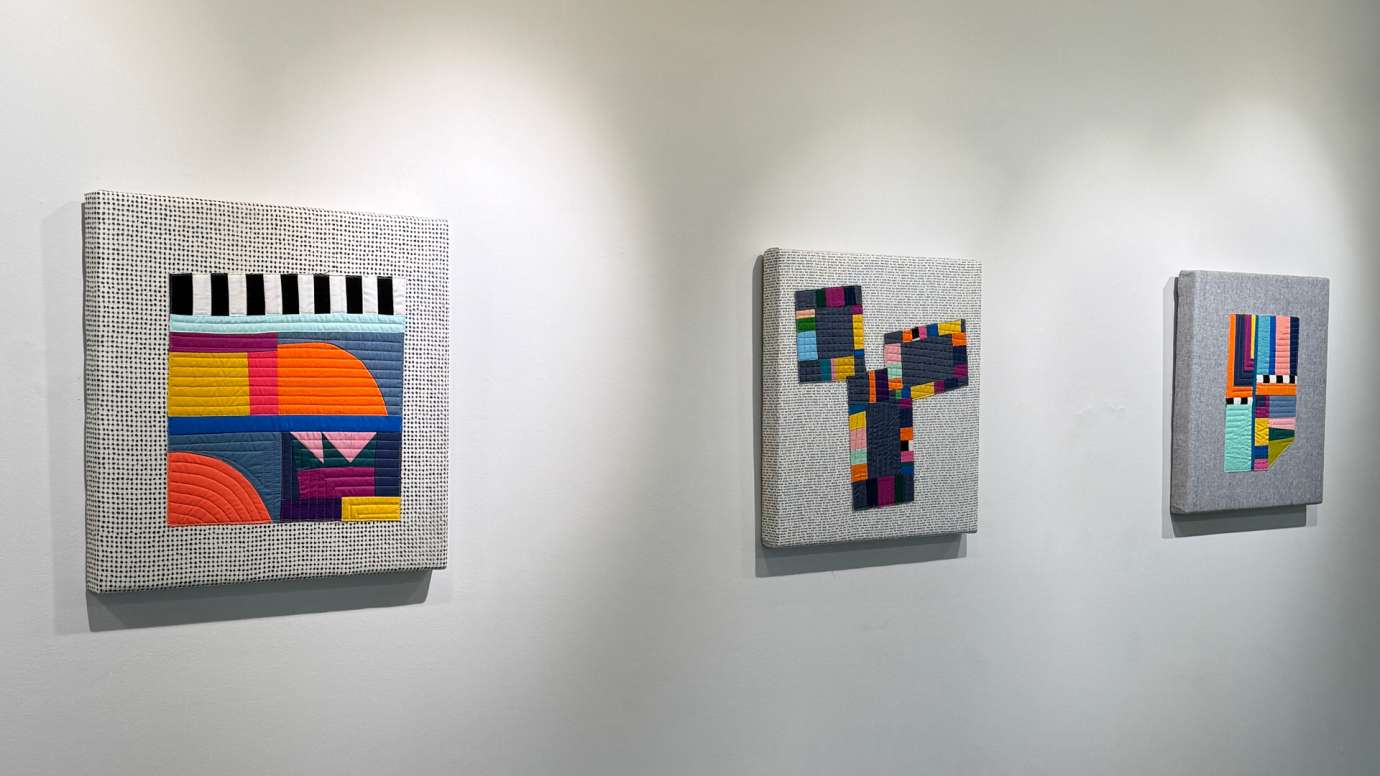 Three colorful, geometric fiber works by Michelle Wilkie hung on a gallery wall