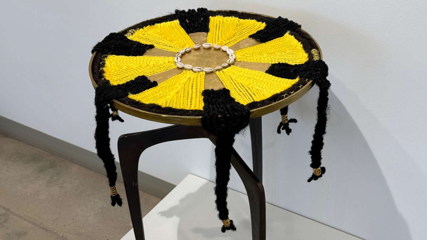 Mixed media sculpture made of repurposed brass table, braiding hair, cowrie shells, metal sun, and gold leaf 