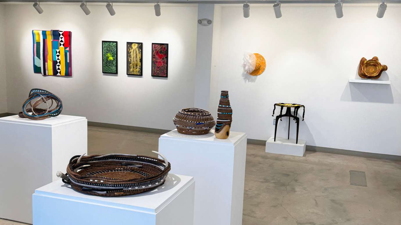 Fiber works by Michelle Wilkie, Mixed media works by Chris-Annia Dobson displayed on one gallery wall with basketry and sculpture by Shakeeka Brookson pedestals