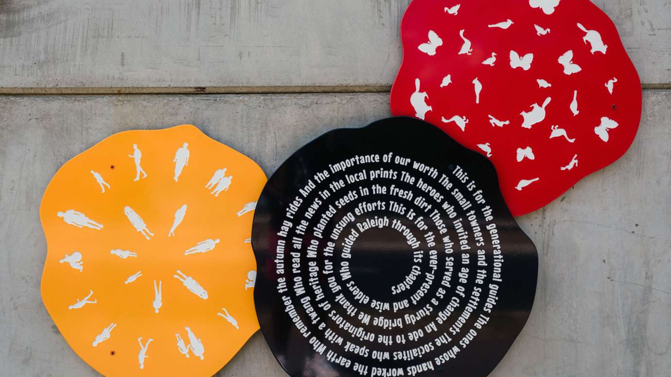 Close up of three metal tree ring discs with shapes and poetry on them