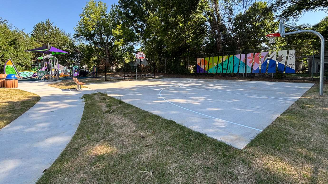 A wide view of a park with playground equipment, a basketball court, and brightly colored artwork