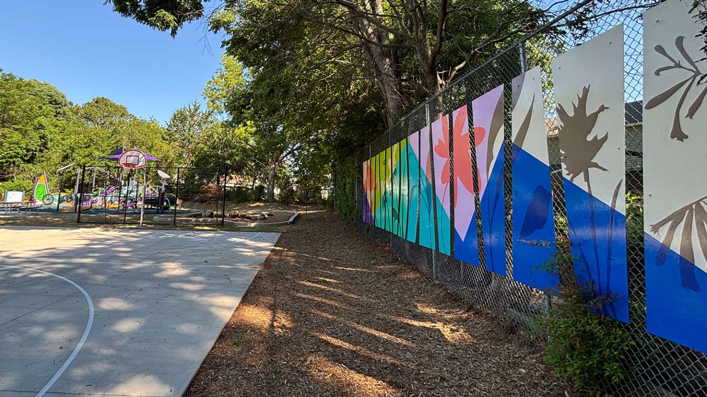 A view looking down a fence line that has bright colored panels on it in a park.