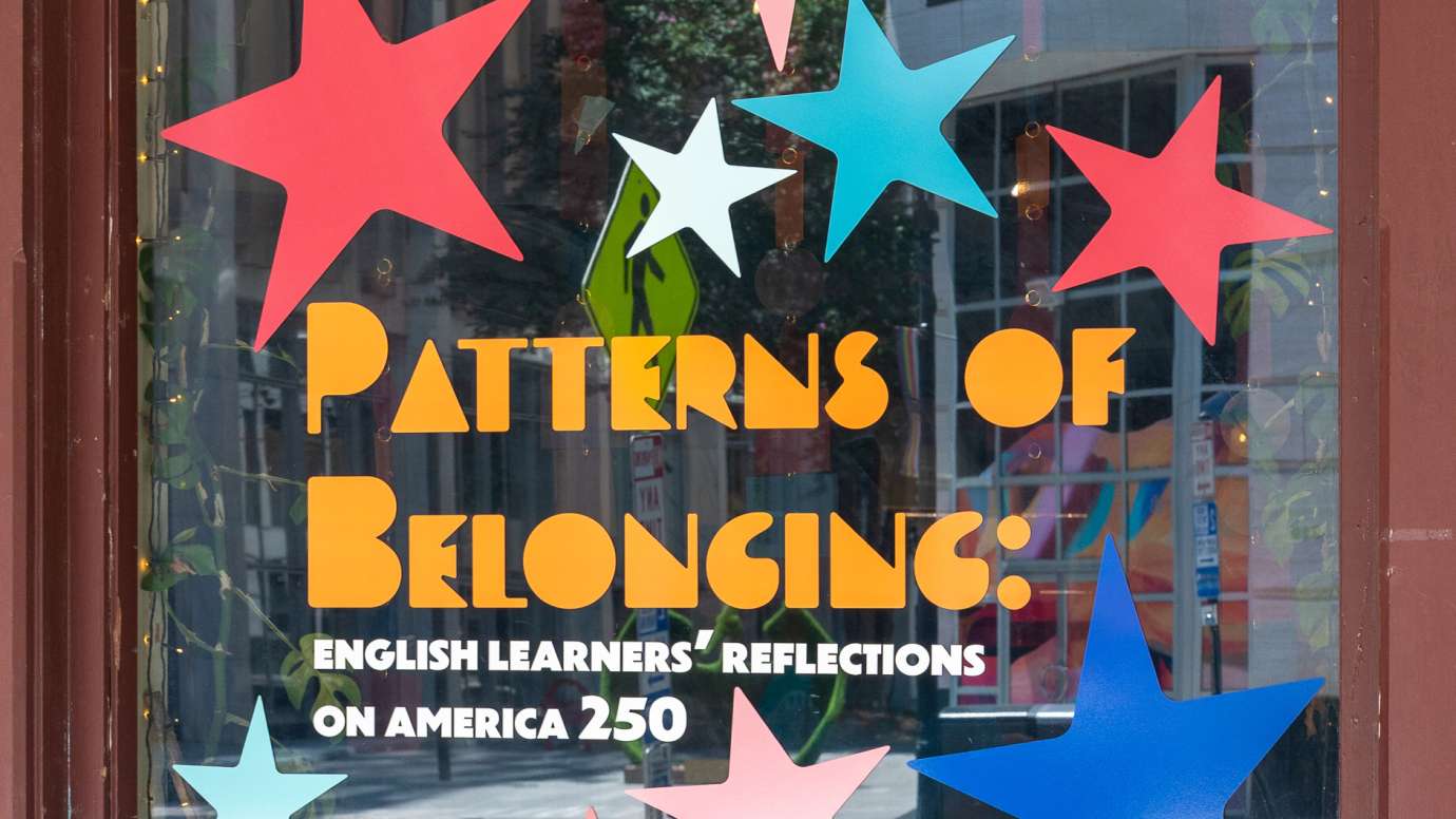 the words "Patterns of Belonging: English Learners' Reflections on America 250" on glass with colorful stars