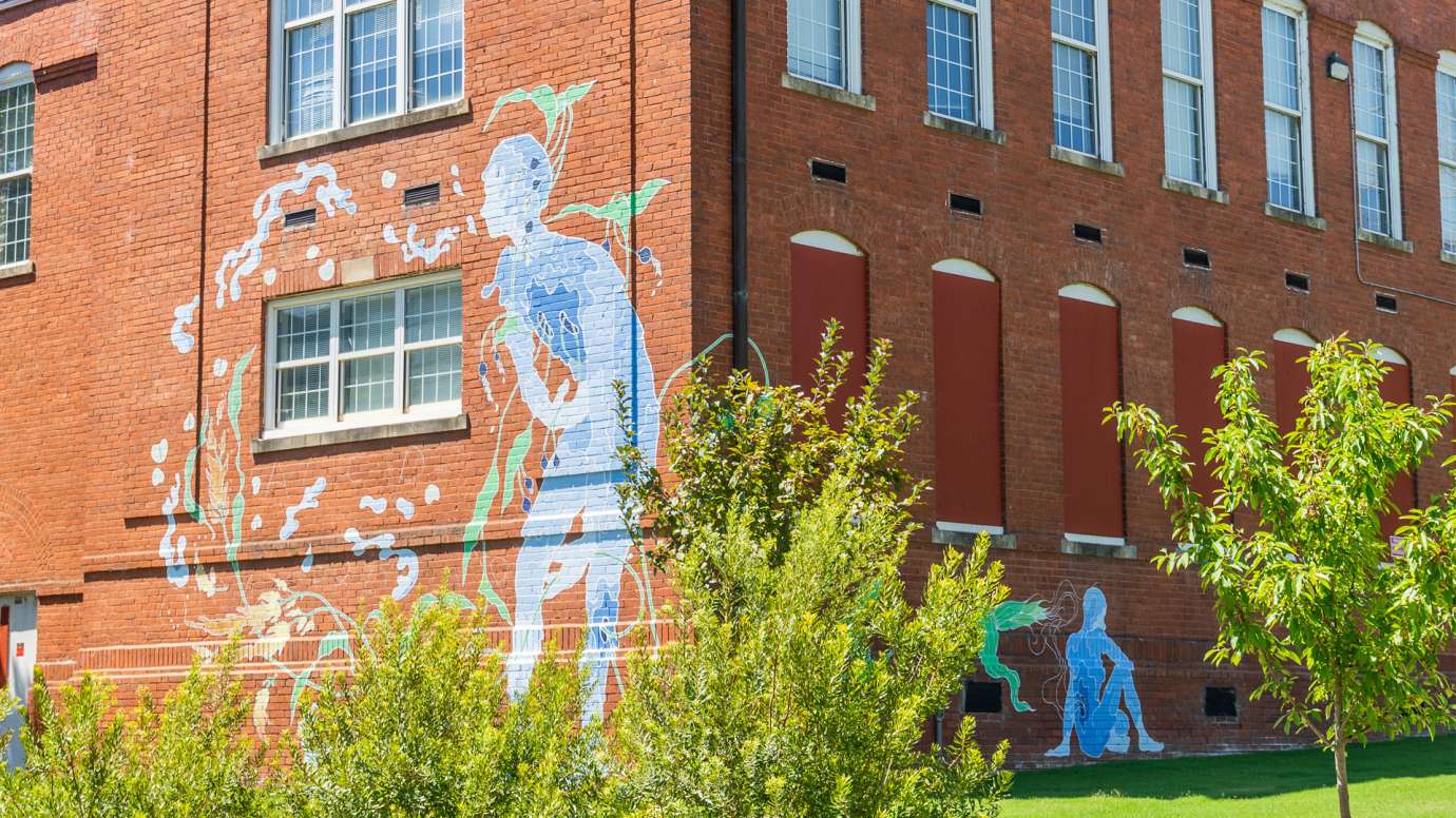 Two watery blue figures are painted on a brick wall with foilage. 