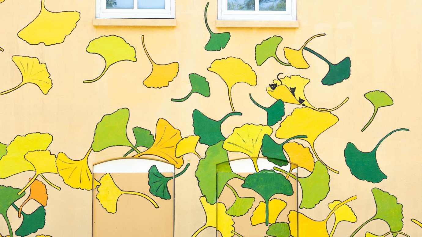 A yellow building is painted with ginkgo leaf shapes in yellow, green, and orange.