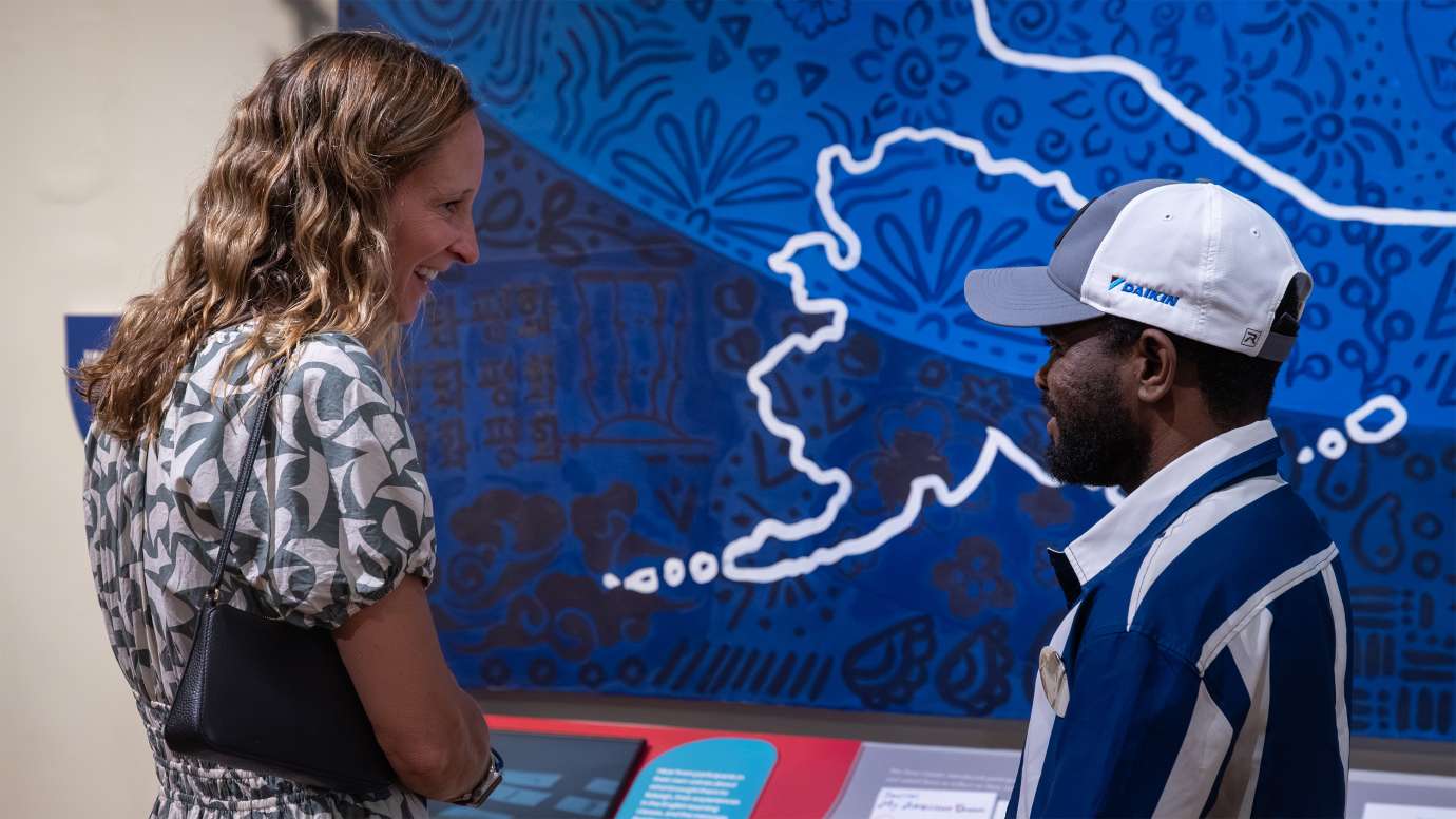 people talking and enjoying an exhibit in front of a blue quilt