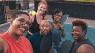 A group of people on a pickleball court with balls and a paddle