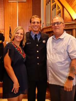  A new fire academy graduate dressed in uniform stands with his parents.