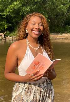 A young woman holds a book and smiles 