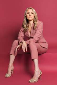Blond woman in a pink suit sitting in a powerful pose.