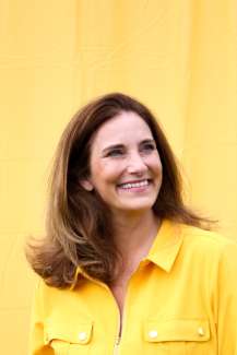 Smiling women with brown hair in a yellow shirt on a yellow background. 